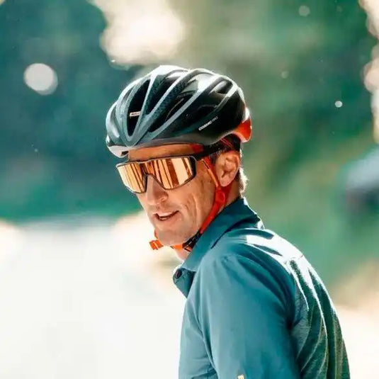 Un cycliste portant un casque noir, une veste bleue et des lunettes de soleil réfléchissantes.